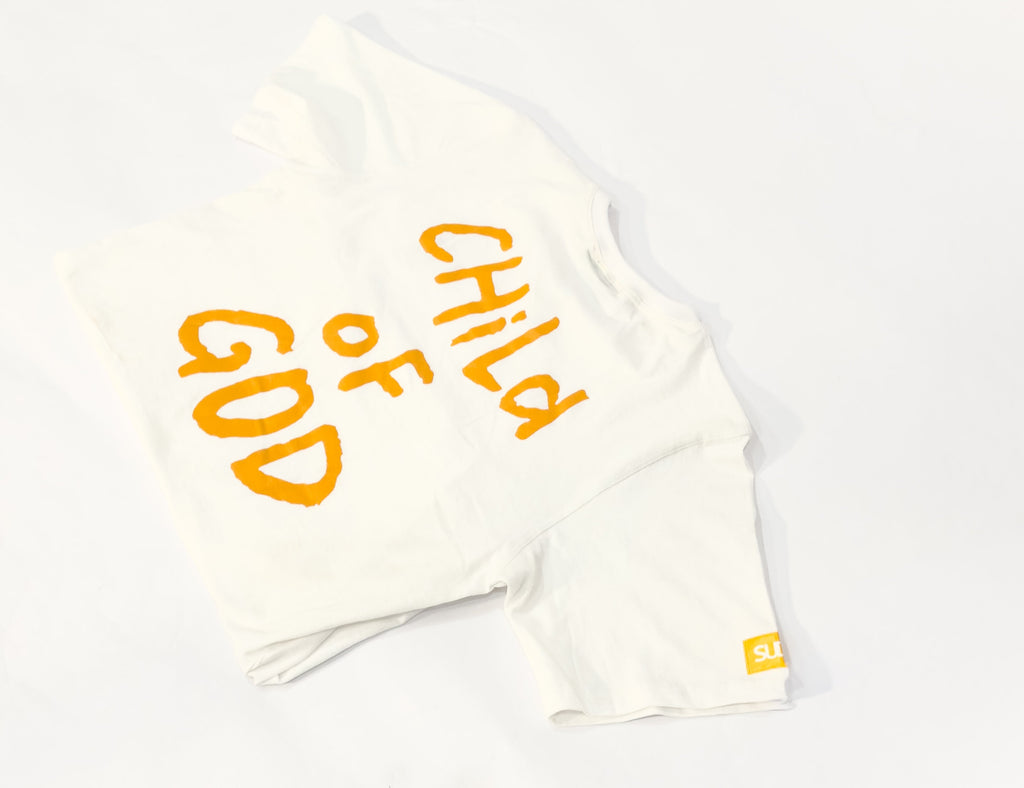 White t-shirt with 'Child of God' text in yellow on a gray surface
