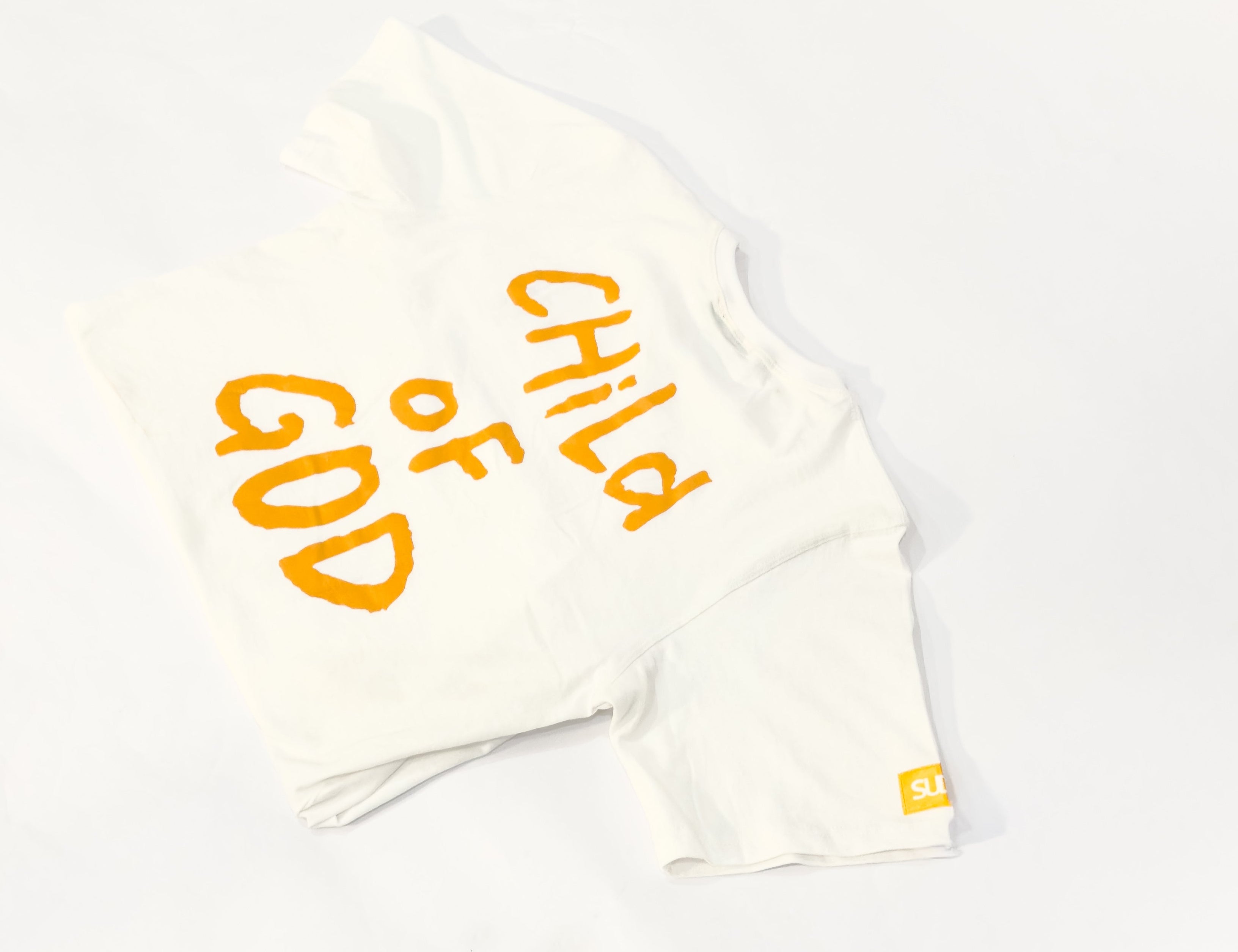 White t-shirt with 'Child of God' text in yellow on a gray surface