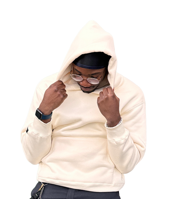 Person wearing a beige hoodie and dark pants on a white background